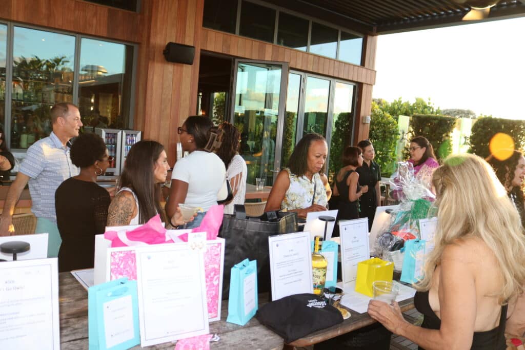 Guests around the raffle and auction item table at the Spirit of Giving Do Good Delray event
